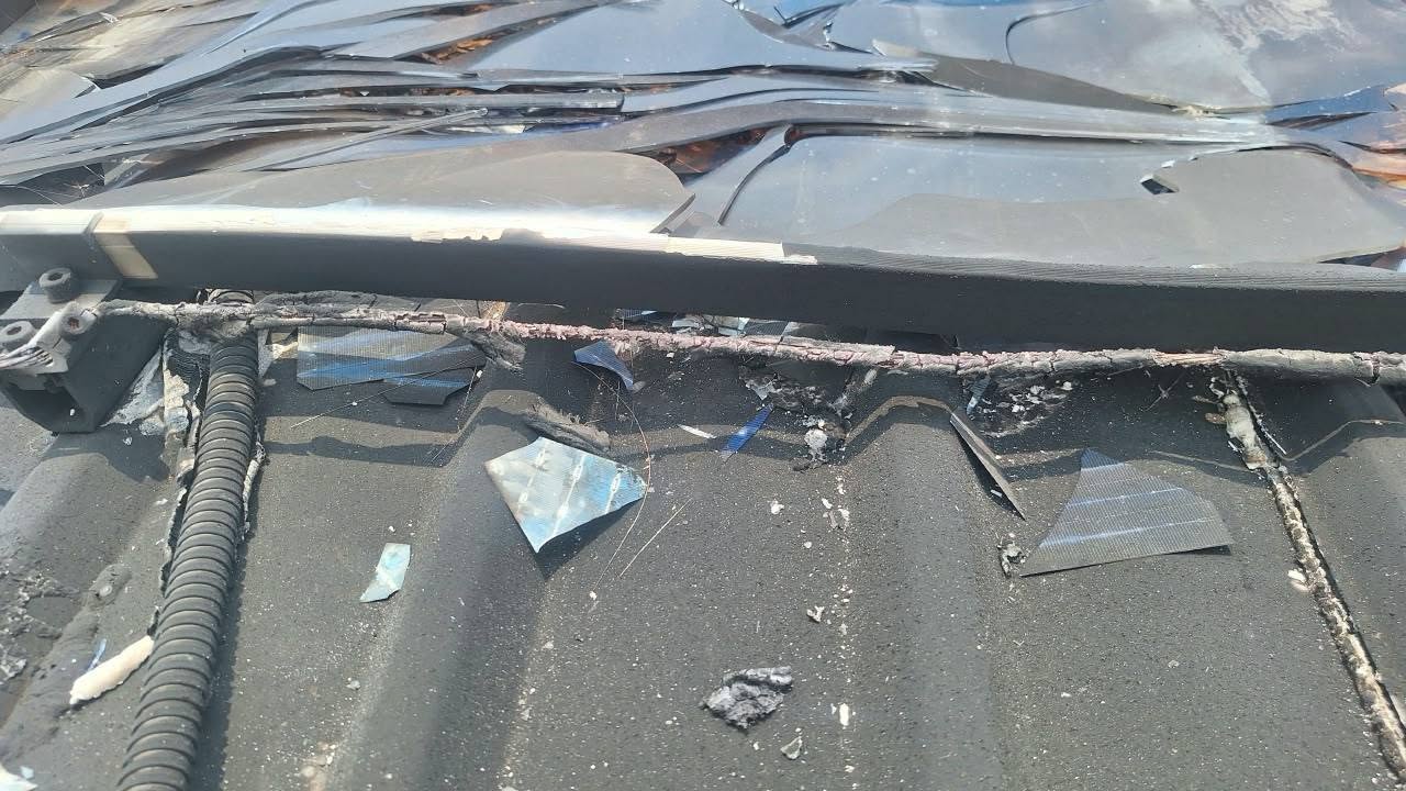 The underside of a burnt module with its backsheet delaminated, and a charred cable running the length of the racking above a metal roof deck