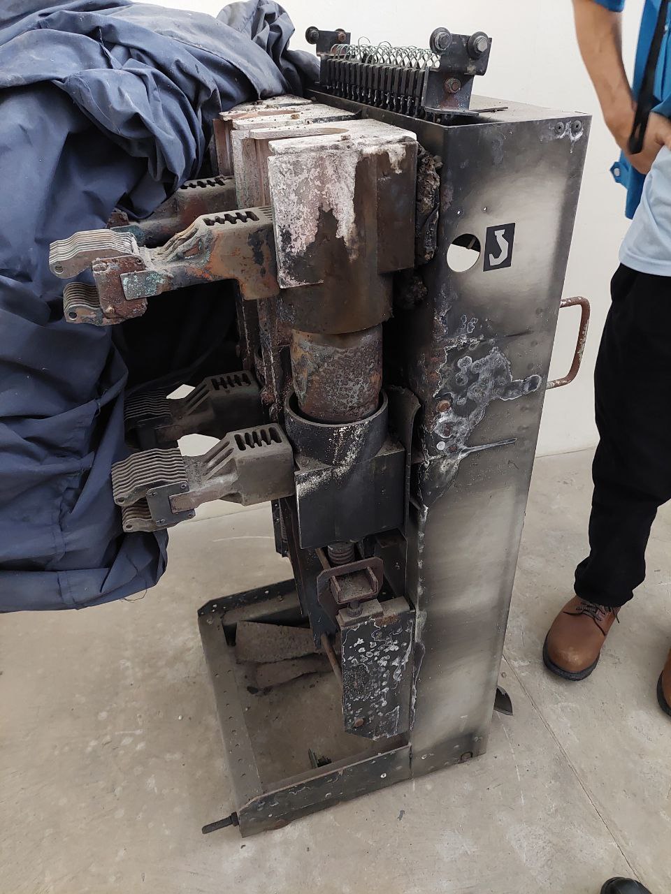 A severely arc-damaged, burnt circuit breaker removed from its panel, standing on the floor