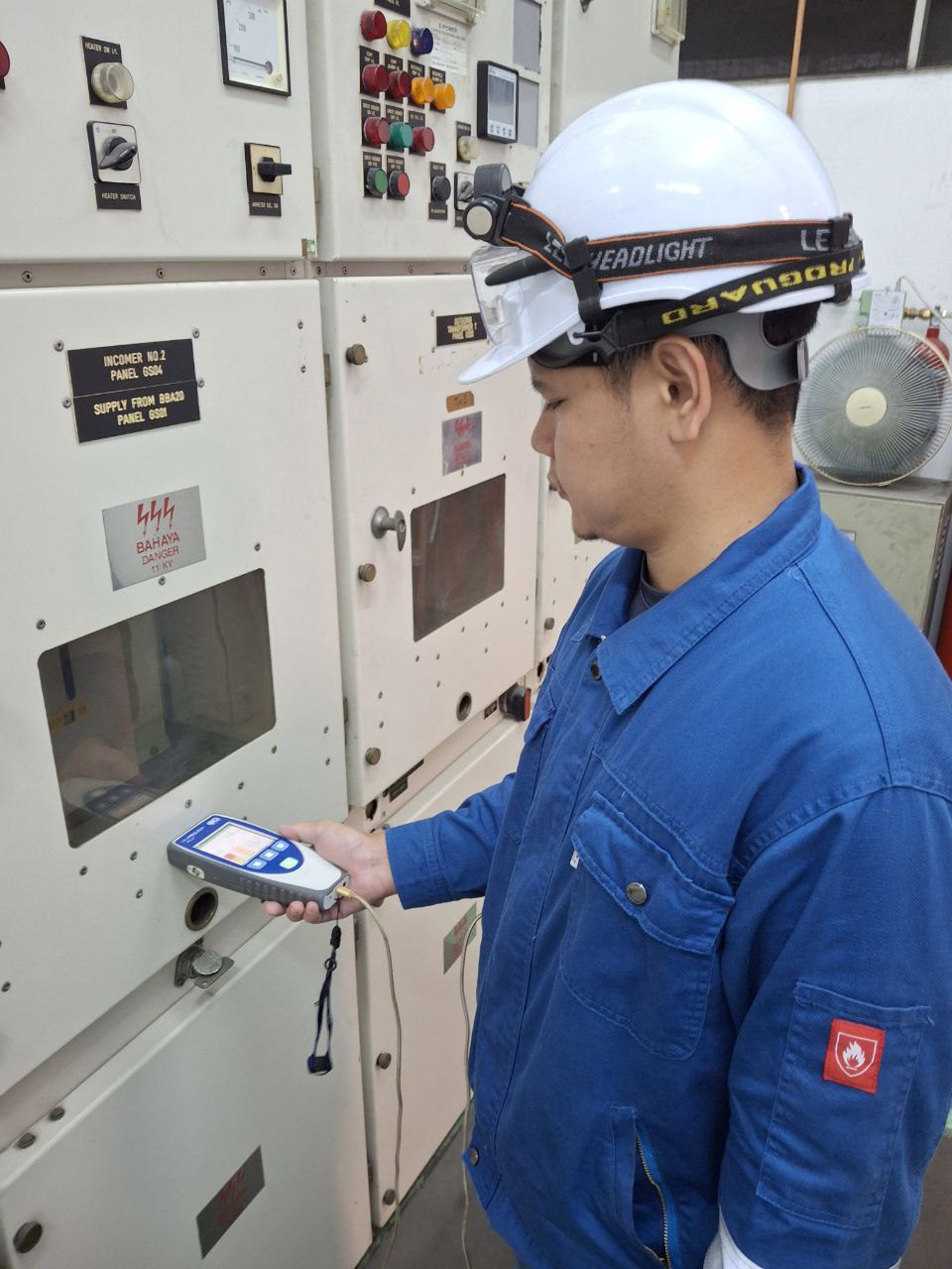 A technician holding a TEV partial discharge detector against live 11 kV switchgear, the panel's danger label visible beside the instrument