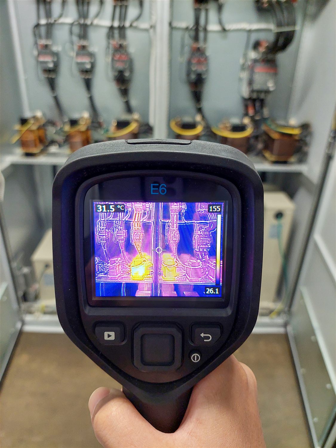 A handheld thermal camera showing the heat pattern of components inside an electrical switchboard