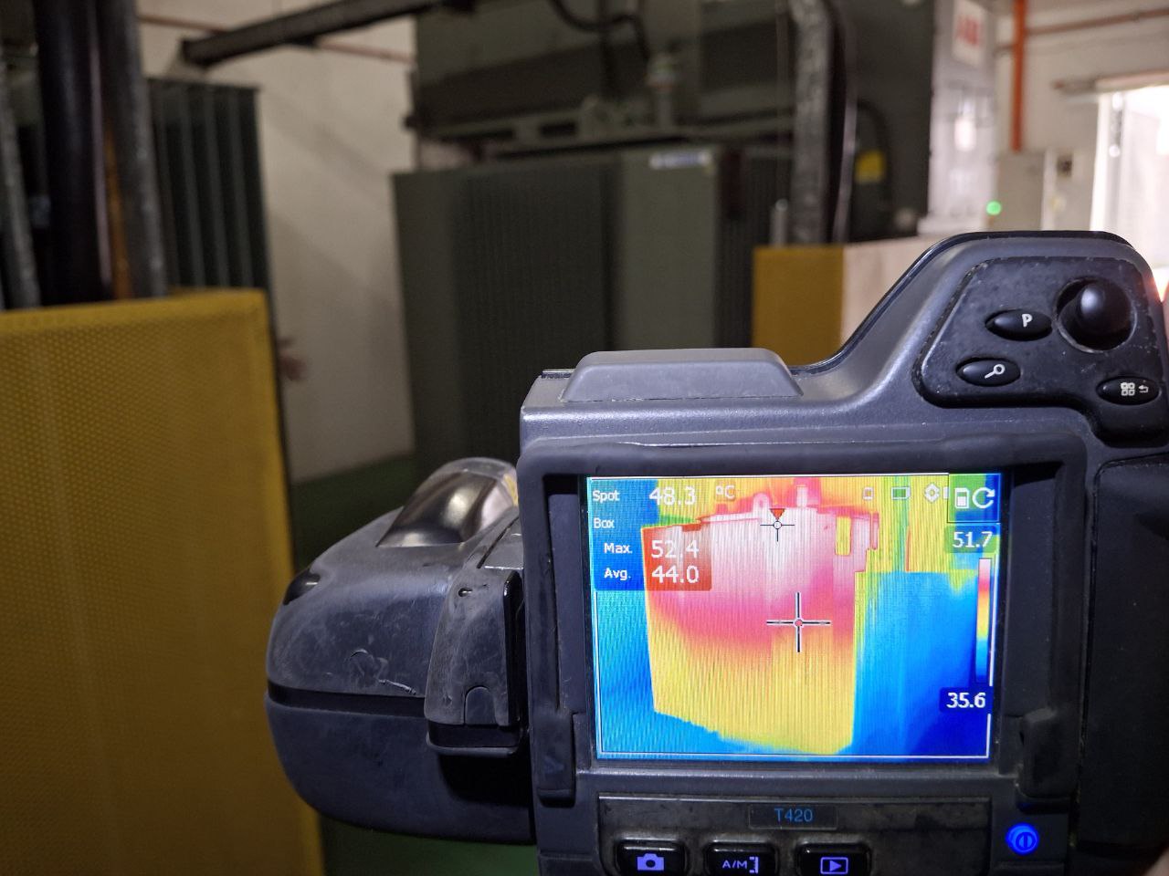 A FLIR T420 thermal camera pointed at a distribution transformer, its screen showing the unit's heat profile with a 52.4 degree maximum